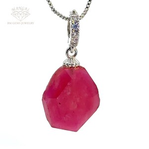 Puede incluir: Un collar con un colgante de plata adornado con una gran piedra preciosa rosa facetada. El colgante está rodeado de pequeñas piedras preciosas transparentes.