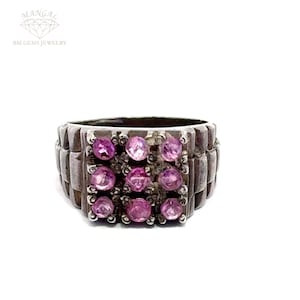 May include: A silver ring with a square-shaped setting featuring nine pink gemstones. The band of the ring has a textured design.