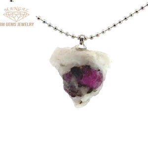 May include: A pendant necklace featuring a raw, irregularly shaped gemstone. The stone is primarily white with a vibrant fuchsia center and dark inclusions. The pendant hangs from a delicate silver ball chain. The brand name "BM GEMS JEWELRY" is visible.