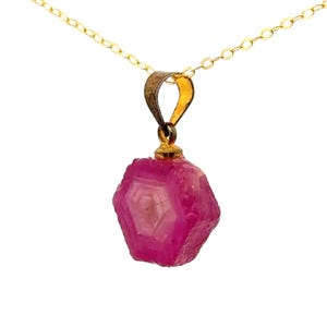 May include: A gold chain necklace with a pink ruby pendant. The ruby is a raw, uncut stone with a hexagonal shape.