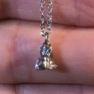 May include: A silver chain necklace with a small, irregular, silver pendant. The pendant is shaped like a rock or a small piece of metal.
