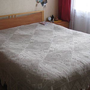 May include: A white crocheted bedspread with a diamond pattern on a wooden bed frame.