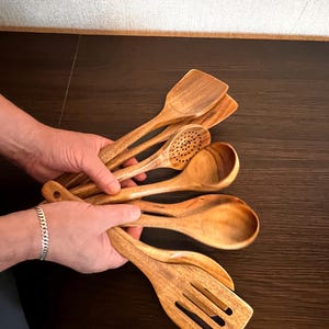 Może przedstawiać: Zestaw drewnianych przyborów kuchennych, w tym szpatułka z otworami, chochla, łyżka i łyżka cedzakowa. Przybory wykonane są z naturalnego drewna i mają ciepły, rustykalny wygląd.