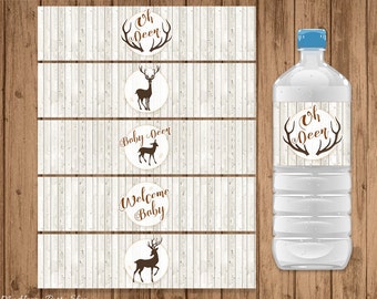 May include: A clear water bottle with a blue cap and a label saying "Oh Deer" with brown antlers. The image also shows matching water bottle labels with deer and text "Baby Deer" and "Welcome Baby" on a wood grain background.