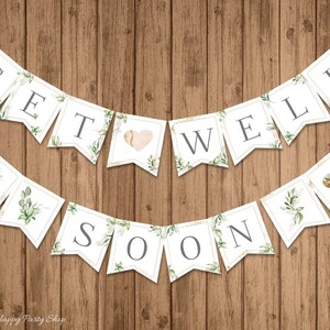 以下が含まれることがあります： 「GET WELL SOON」の文字が印刷された白いペナントのバナー。各ペナントは緑の葉と金のトリムで装飾されています。一部のペナントにはハートの形が描かれています。バナーは木製の背景に表示されています。