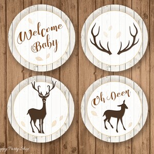 May include: Four circular baby shower decorations with a rustic theme. Each circle has a white wood grain background with brown text and accents. The text includes "Welcome Baby" and "Oh Deer", along with deer and antler silhouettes.