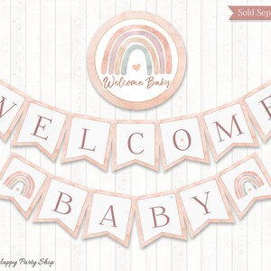 May include: Welcome Baby banner with pink and white pennants featuring the words "Welcome Baby" and a rainbow design. The banner is decorated with small gold stars.