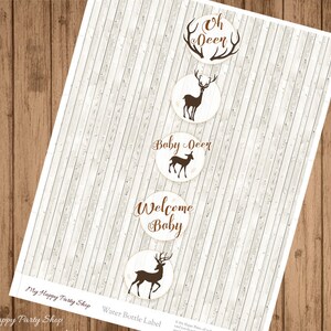 May include: Water bottle labels with a woodland theme. The labels are circular with a light beige background and brown text and deer silhouettes. Text includes "Oh Deer", "Baby Deer", and "Welcome Baby". The labels are on a sheet with a light wood grain background.