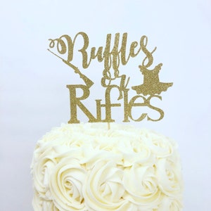 May include: Gold glitter cake topper with the text "Ruffle & Rifles" and a silhouette of a ballerina and a rifle.