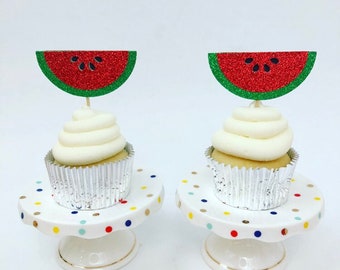 Könnte beinhalten: Zwei Cupcakes mit weißem Frosting, verziert mit roten und grünen Glitzer-Wassermelonen-Cupcake-Toppern. Die Cupcakes stehen auf weißen Kuchenständern mit bunten Punkten.