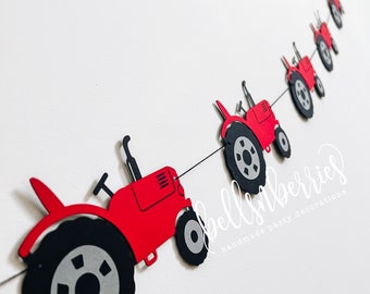 May include: Red paper tractor garland with black wheels and gray tire treads. The garland is strung together with twine and has the text "bells&berries handmade party decorations" at the bottom.