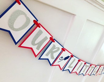 Könnte beinhalten: Ein rot-weiß-blaues Banner mit silbernen Glitzerbuchstaben, auf dem "Our Little Firecracker" steht.