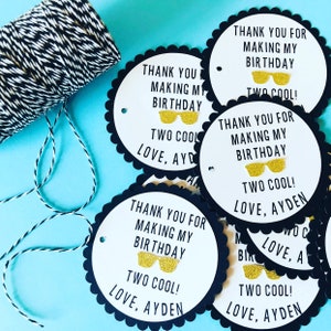 May include: Black and white circular thank you tags with white text that reads "Thank you for making my birthday two cool! Love, Ayden". The tags have a scalloped edge and a gold glitter pair of sunglasses.