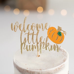 May include: Gold glitter cake topper with the text "welcome little pumpkin" and a small orange pumpkin with a green leaf.