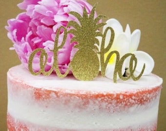 May include: A white and pink layered cake with a gold glitter pineapple and "Aloha" topper. The cake is decorated with pink and white flowers.