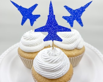 May include: Three cupcakes with white frosting and blue glitter jet plane toppers.