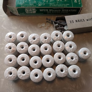 May include: A collection of white ceramic WP22E Wisconsin insulators with the text "USA" and "22" stamped on them. The image also shows a box of nails and a box with the text "WP22E Wisconsin INSULATORS".