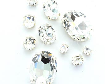 Owalne kamienie Swarovski i Preciosa w oprawach do przyszywania. Kamienie są kryształowe, a oprawy do przyszywania są posrebrzane