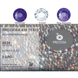 Könnte beinhalten: Nahaufnahme von drei facettierten Kristall-Strasssteinen in den Farben Heliotrop, Kristall und Deep Tanzanite. Das Bild zeigt auch ein Etikett mit dem Text "PRECIOSA 438 11 612", "SS34 CRYSTAL" und "SILVER FOILED". Der Markenname "PRECIOSA" ist ebenfalls sichtbar.