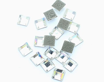 Puede incluir: Una dispersión de piedras de cristal cuadradas transparentes con facetas iridiscentes, algunas con respaldo gris, sobre una superficie blanca.