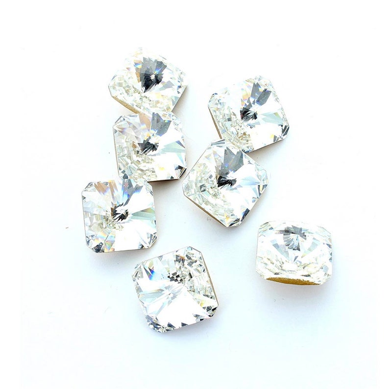 May include: Eight clear square-shaped crystal rhinestones with a faceted design.
