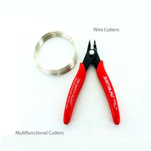 May include: Red wire cutters with the text "JUSTINLAU" and "USE SAFETY GLASSES" on the handles. The cutters are next to a coil of silver wire.
