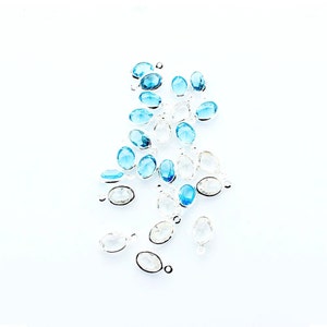 May include: A collection of oval-shaped gemstone beads with silver jump rings. The beads are a mix of clear and light blue.