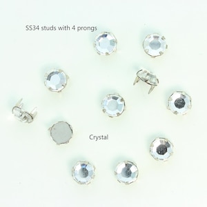 May include: A close-up of ten clear crystal studs with four prongs each. The studs are arranged in a circle on a white background. The text "SS34 studs with 4 prongs" and "Crystal" are visible in the image.