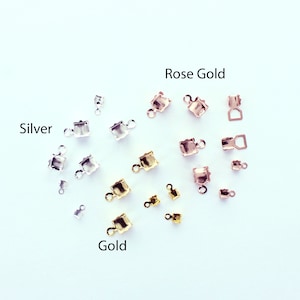 May include: Assortment of silver, rose gold, and gold metal clasps for jewellery making. The clasps are square shaped with a small loop on each side.