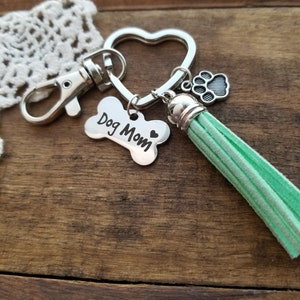 May include: A silver heart-shaped keychain with a bone-shaped charm that says "Dog Mom" and a small paw print charm. The keychain has a green tassel.