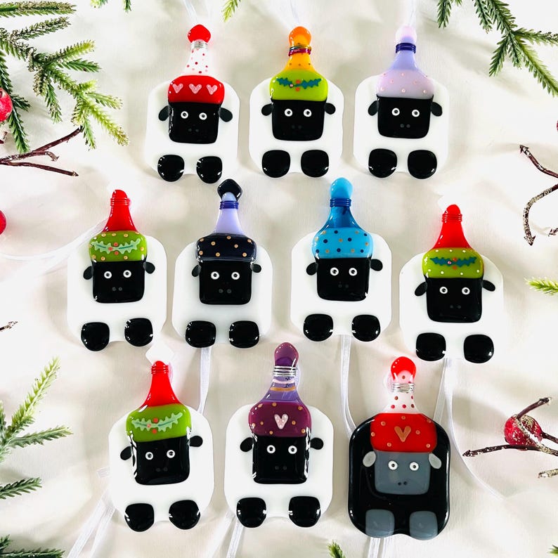 Puede incluir: Nueve adornos de vidrio con forma de oveja, cada uno con un sombrero festivo diferente. Los sombreros est&aacute;n decorados con varios colores, patrones y dise&ntilde;os, incluyendo rojo, verde, azul, morado y dorado. Las ovejas tienen caras y patas negras.