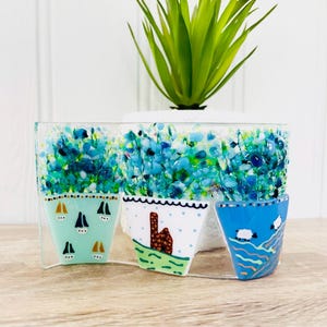 May include: A decorative glass piece featuring three potted plants with different designs. The plants are surrounded by blue and green glass mosaic tiles. The piece is perfect for adding a touch of whimsy to any home.