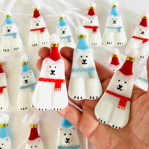 以下が含まれることがあります： 手作りのガラス製のオーナメントのセット。ホッキョクグマが、お祝いの帽子とマフラーを身につけています。オーナメントは白地に赤と青のアクセントが施され、幻想的で魅力的なデザインです。
