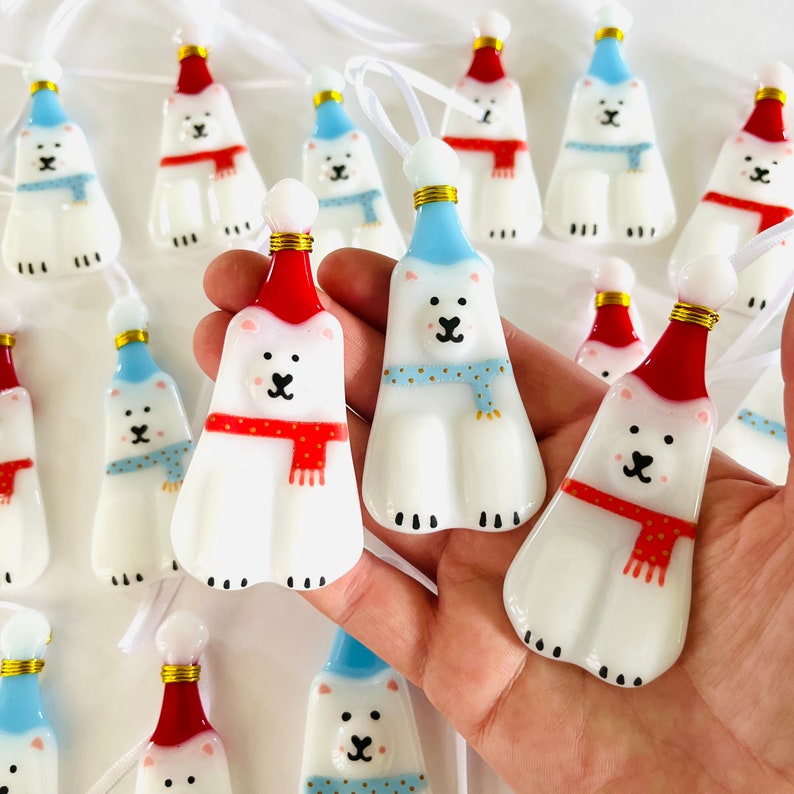 以下が含まれることがあります： 手作りのガラス製のオーナメントのセット。ホッキョクグマが、お祝いの帽子とマフラーを身につけています。オーナメントは白地に赤と青のアクセントが施され、幻想的で魅力的なデザインです。