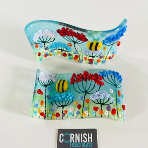 May include: Two blue glass panels with a wavy design. The panels feature a floral design with red, yellow, white, and blue flowers. The panels also feature bees with black and yellow stripes. The panels are labeled "CORNISH FUSED GLASS".
