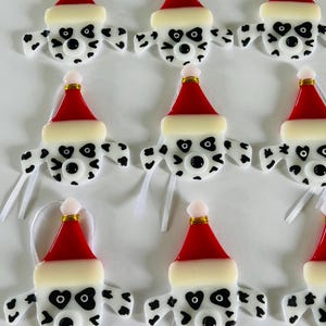 May include: Ten handmade glass ornaments featuring Dalmatian dog faces wearing Santa hats. The ornaments are white with black spots and have red and white Santa hats.