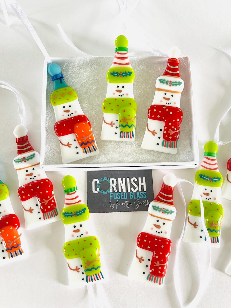 K&ouml;nnte beinhalten: Handgefertigte Schneemann-Ornamente aus verschmolzenem Glas. Jedes Ornament ist wei&szlig; mit einem bunten Schal, Hut und Kn&ouml;pfen. Die Ornamente werden in einer wei&szlig;en Schachtel pr&auml;sentiert und sind fertig zum Aufh&auml;ngen. Die Ornamente sind etwa 10 cm hoch.