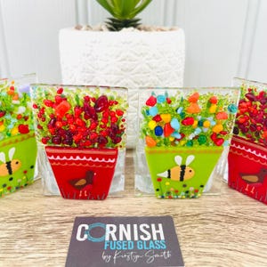May include: Four small glass flower pot ornaments with colourful flowers and bees. The pots are red, green and white. The ornaments are made by Cornish Fused Glass by Kirsty Smith.
