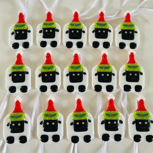 Puede incluir: Doce adornos de vidrio blanco con forma de oveja que llevan gorros de Pap&aacute; Noel rojos y verdes. Los adornos tienen ojos negros y una nariz negra.