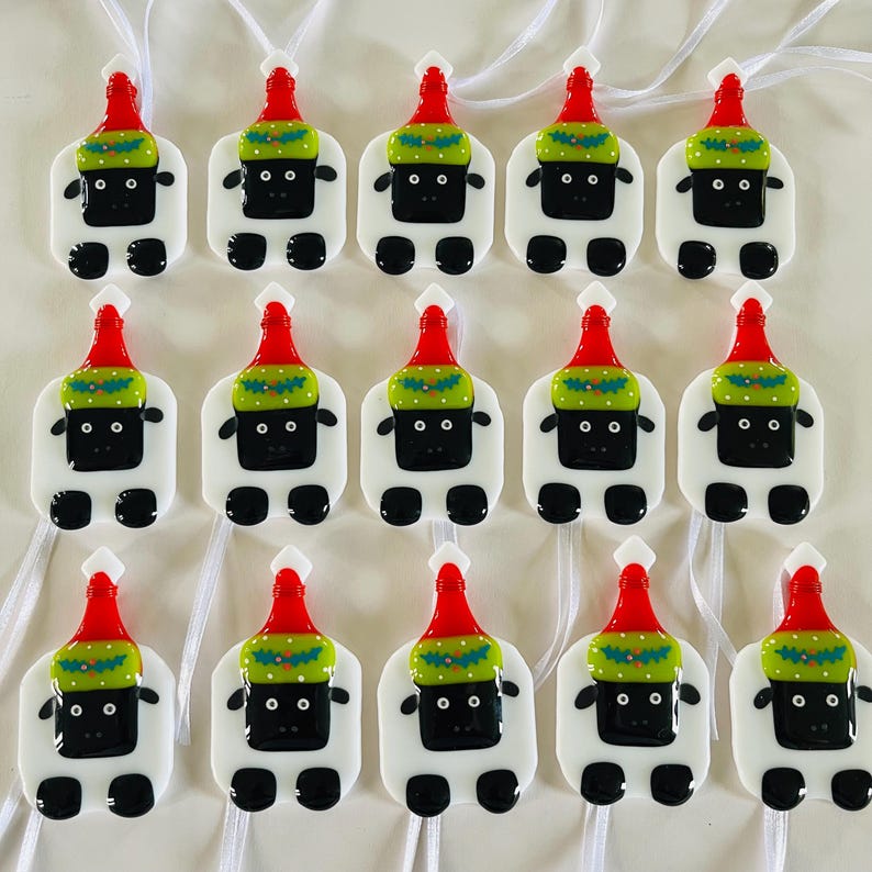 Puede incluir: Doce adornos de vidrio blanco con forma de oveja que llevan gorros de Pap&aacute; Noel rojos y verdes. Los adornos tienen ojos negros y una nariz negra.