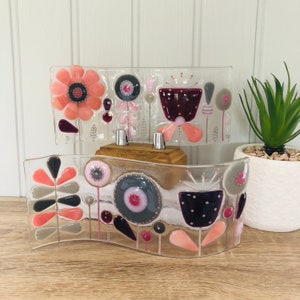May include: Two glass panels with a wavy, abstract floral design. The top panel is rectangular and features pink, grey, and purple flowers. The bottom panel is curved and features pink, grey, and purple flowers.