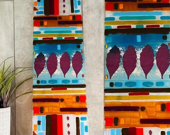 May include: Two colorful abstract glass wall art pieces with geometric patterns and purple leaf designs. The pieces are made of stained glass and have a mosaic look.