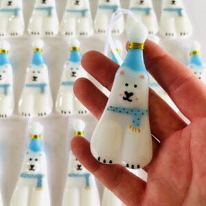 以下が含まれることがあります： 青い帽子とマフラーをつけたシロクマの形をした白いガラスのオーナメントのセット。オーナメントは金色のアクセントが付いており、クリスマスツリーの飾り付けに最適です。