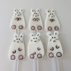 Può includere: Sei ornamenti in vetro bianco a forma di topo con piedi rosa e occhi neri. Gli ornamenti sono su bastoncini trasparenti.