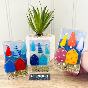 May include: Fused glass art pieces depicting colorful seaside scenes with houses, trees, and seagulls. The artwork features vibrant hues of red, blue, yellow, and purple. The pieces are rectangular and appear to be decorative items.