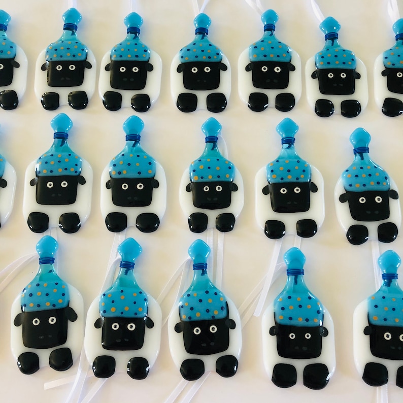 Puede incluir: Una colecci&oacute;n de adornos de ovejas blancas con sombreros de fiesta azules y dorados. Cada oveja tiene ojos negros y una nariz negra. Los adornos cuelgan de cintas blancas.