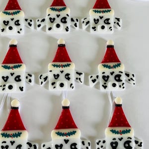 May include: Eight white and black Dalmatian dog ornaments with red and green Santa hats. The ornaments are made of glass and have a white background with black spots. Each ornament has a loop for hanging.