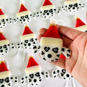 May include: A set of handmade glass ornaments featuring Dalmatian dog faces wearing Santa hats. The ornaments are white with black spots and have black eyes and noses. Each ornament has a white ribbon for hanging.