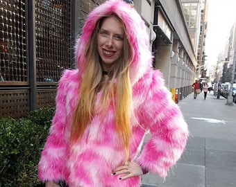 Puede incluir: Una chaqueta de piel sintética rosa y blanca con capucha. La chaqueta tiene un patrón a rayas y la lleva puesta una persona con el pelo largo y rubio.