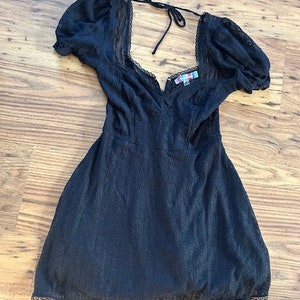Peut inclure: Une robe en dentelle noire avec un d&eacute;collet&eacute; en c&oelig;ur et des manches bouffantes. La robe a un n&oelig;ud &agrave; l'arri&egrave;re du cou.